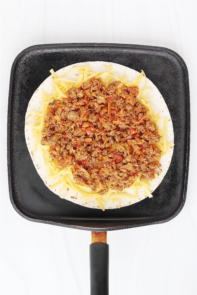 Overhead photo of a pan with a tortilla, shredded cheese with sloppy joe mixture.