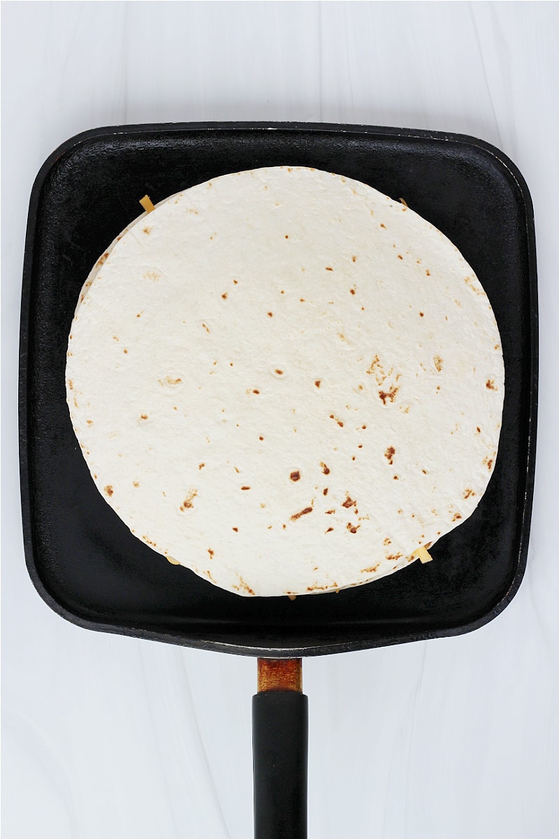 Overhead photo of a sloppy joe quesadilla on a flat black stovetop pan.