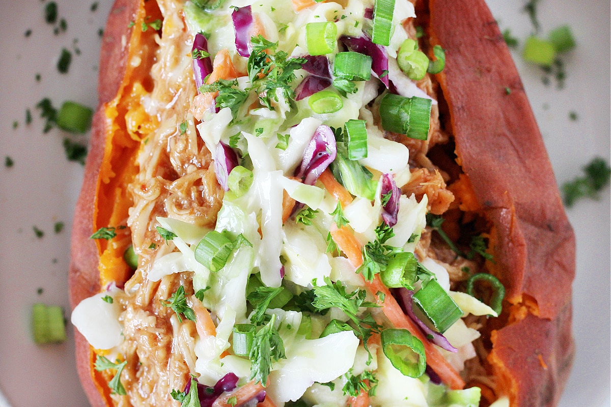Overhead photo of a sweet potato layered with BBQ chicken, coleslaw, green onion and parsley.