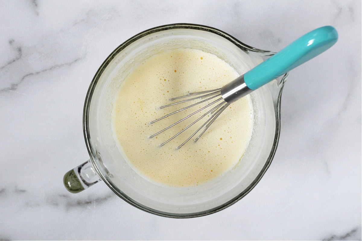 Melted butter, milk and eggs whisked together in a glass mixing bowl.