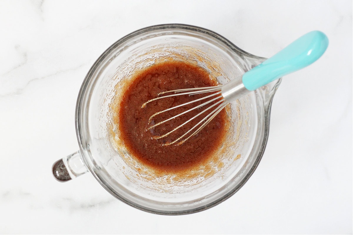 A whisk stirring cinnamon, sugar and butter in a glass bowl.