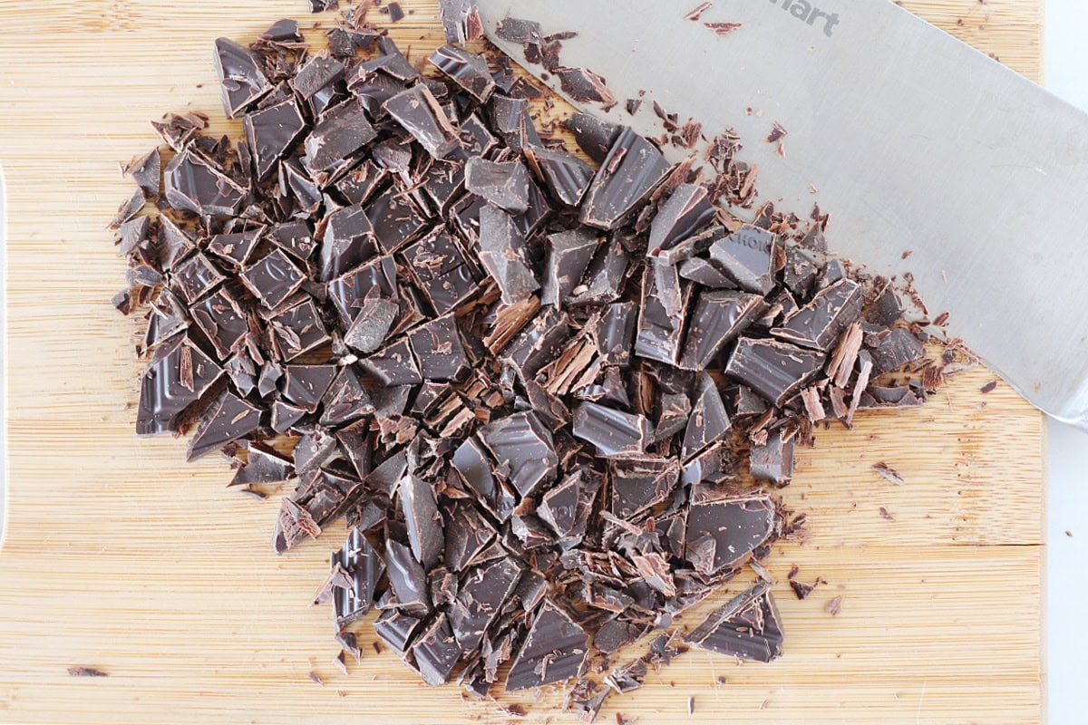 A dark chocolate bar cut into pieces with a knife on a cutting board.