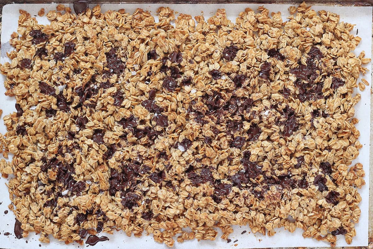Overhead photo of dark chocolate pieces melting into a pan of warm granola.