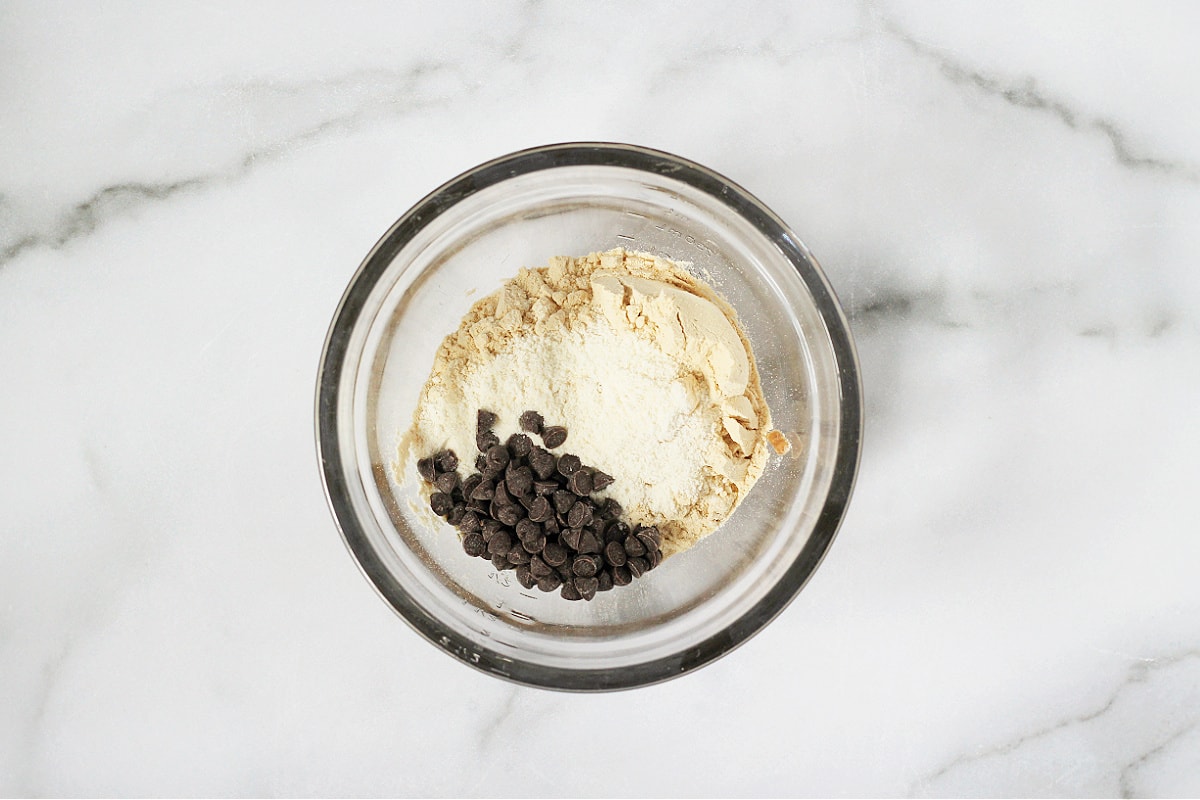 Overhead photo of a bowl with vanilla protein powder, coconut flour, and chocolate chips.