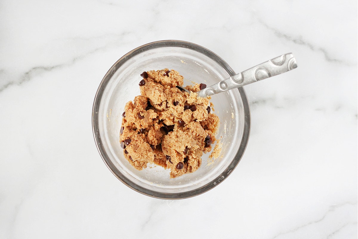 A spoon mixing together the ingredients for high protein cookie dough bark in a bowl.