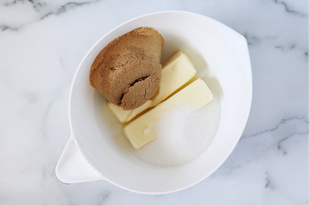 Brown sugar, white sugar and butter sticks in a white mixing bowl.