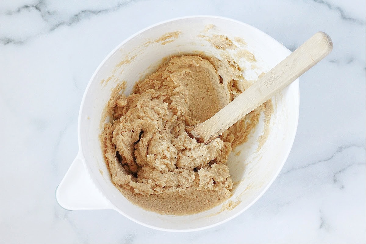 A wooden spoon creaming butter and sugar together in a white mixing bowl.