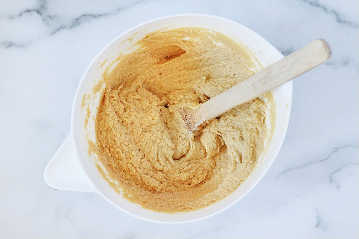 A wooden spoon sitting in the wet ingredients in a white mixing bowl.