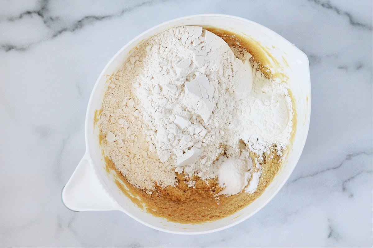 Flour, cornstarch and baking soda sitting on the wet ingredients in a white bowl.