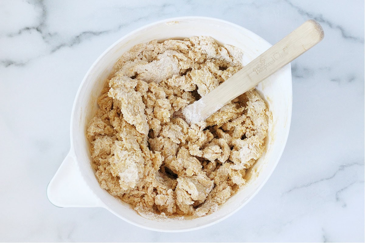 A wooden spoon mixing flour into a cookie dough batter.