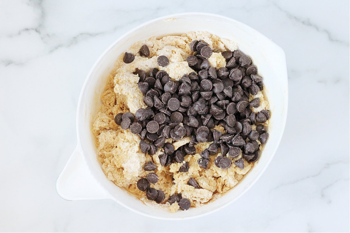 Dark chocolate chips on cookie dough batter in a white mixing bowl.