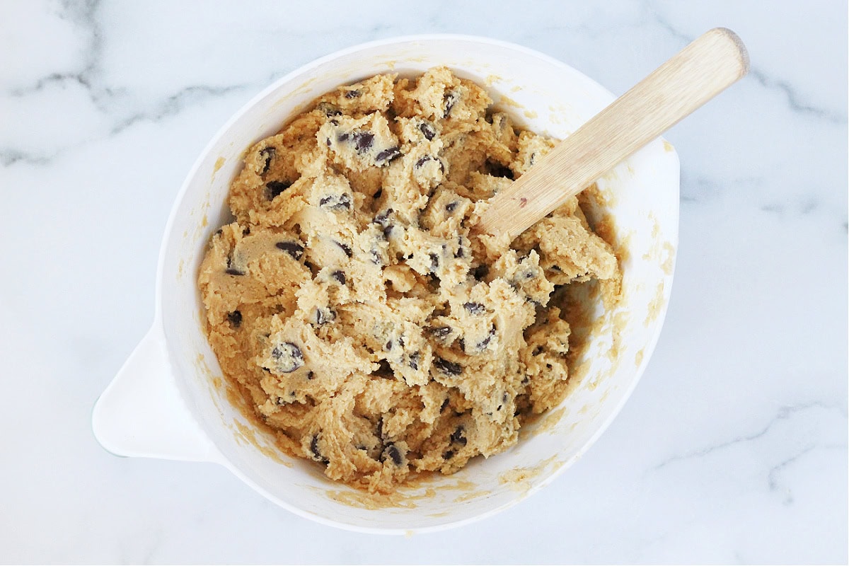 Overhead photo of chocolate chip cookie dough batter on a white mixing bowl.