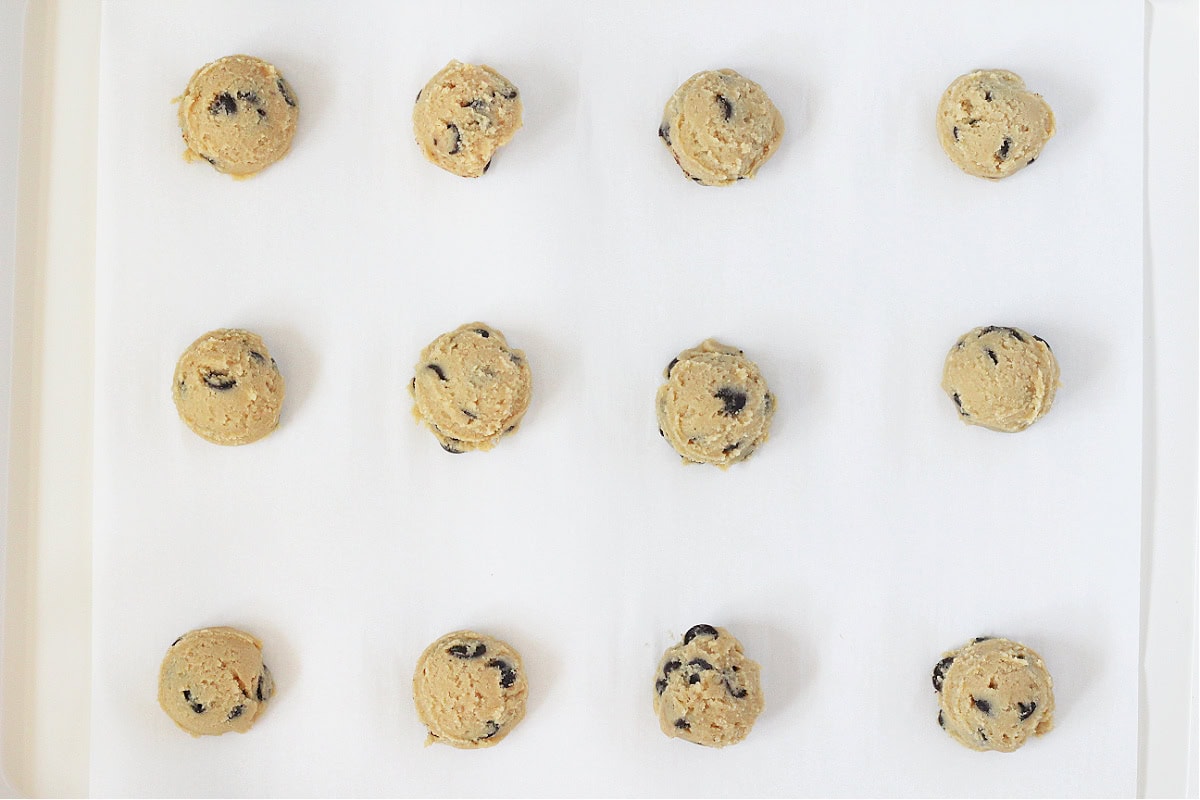 Twelve chocolate chip cookie dough balls on a baking sheet.