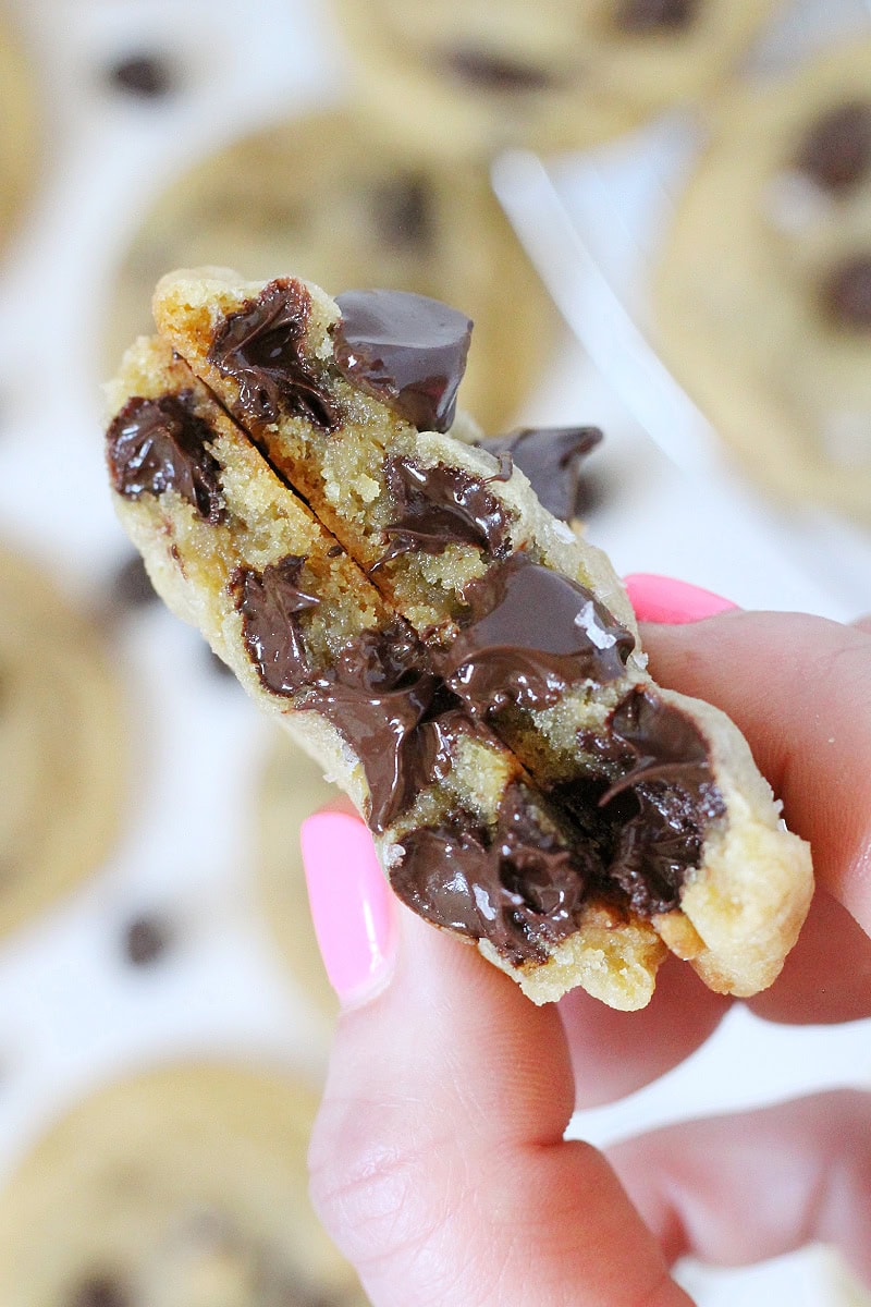 Two halves of a warm cookie with melting chocolate chips held by a woman's hand.