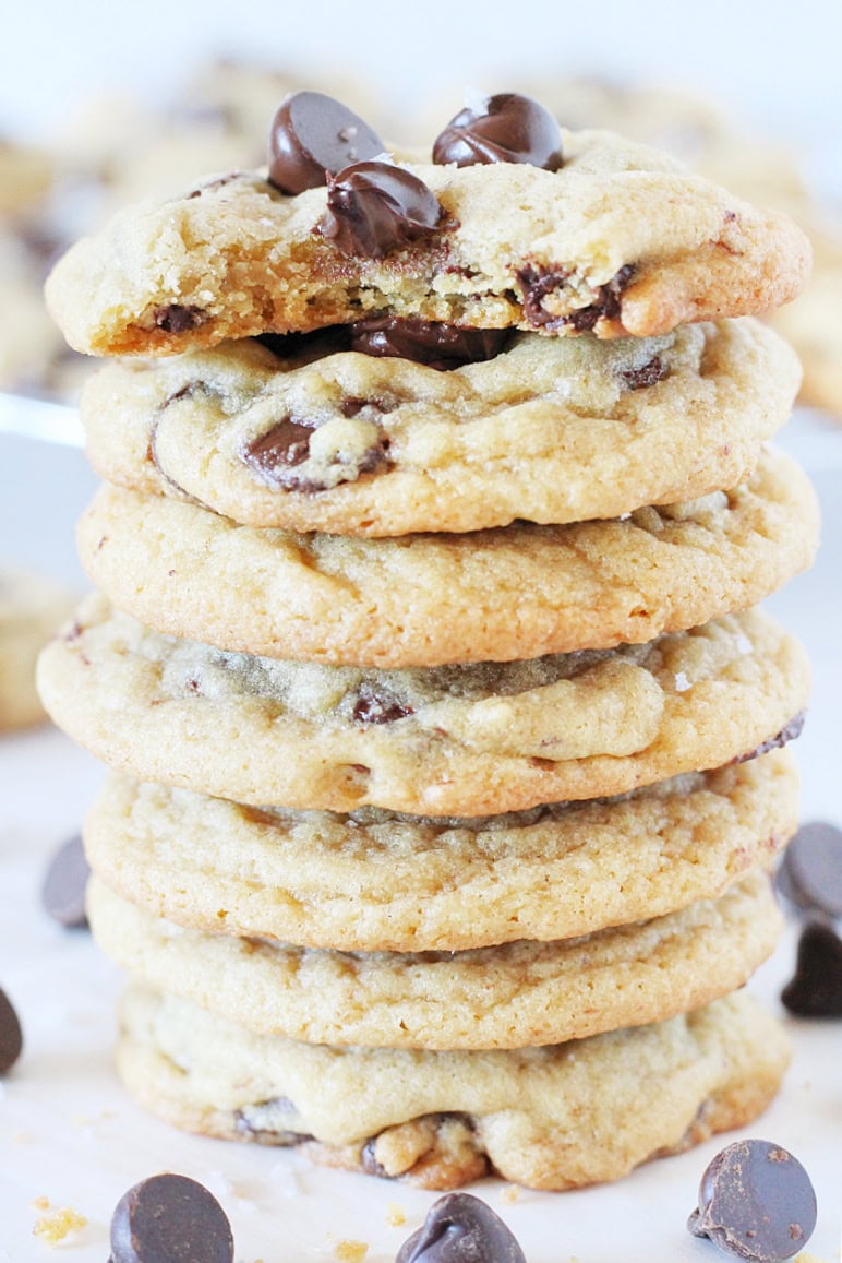 A stack of seven homemade chocolate chip cookies with a bite taken out of one.