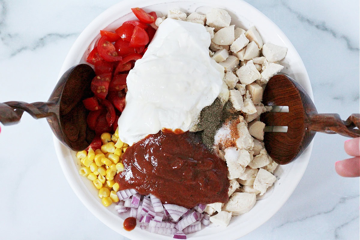 Overhead photo of diced chicken, sour cream, bbq sauce and veggies in a white bowl.