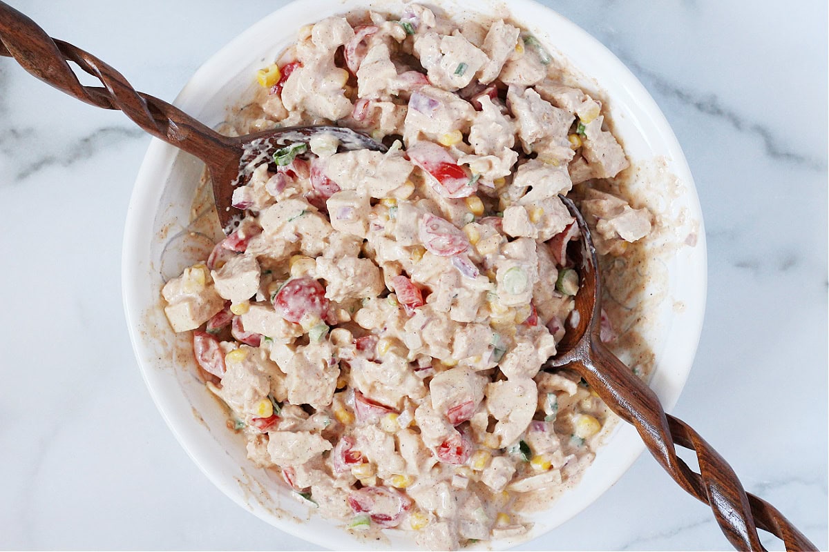 Overhead photo of creamy bbq chicken salad in a bowl with two wooden spoons.