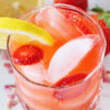 Overhead photo of pink lemonade in a glass with ice, lemon wedge and sliced strawberries.