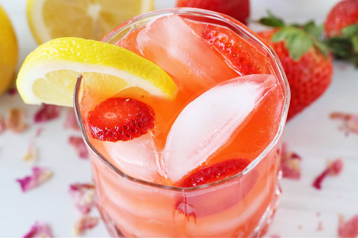 Overhead photo of pink lemonade in a glass with ice, lemon wedge and sliced strawberries.