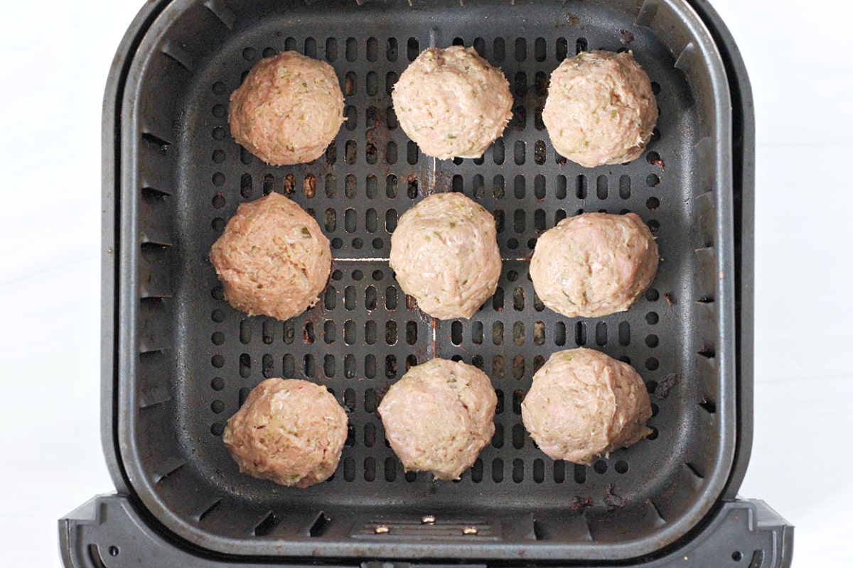 Overhead photo of unbaked turkey pesto meatballs in an air fryer basket. 