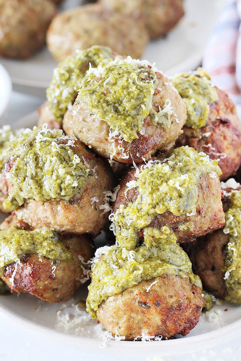 Turkey Pesto Meatballs stacked on a plate topped with basil pesto and Parmesan cheese.