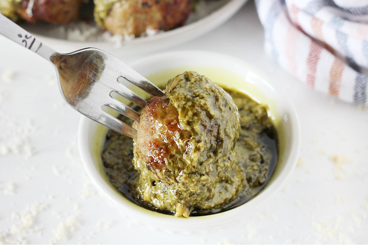 A fork dipping an air fryer meatball in a bowl of basil pesto. 