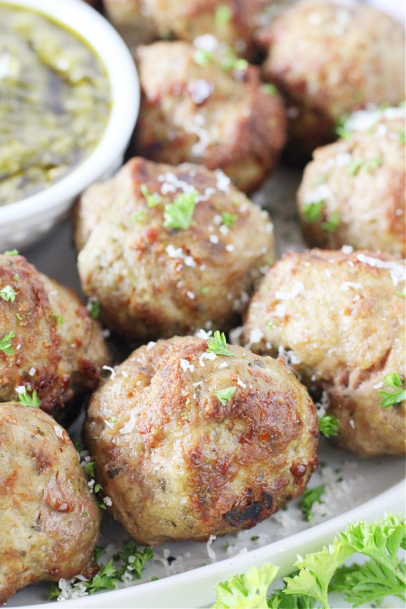 Up close air fryer turkey pesto meatballs topped with chopped parsley and shredded parmesan.