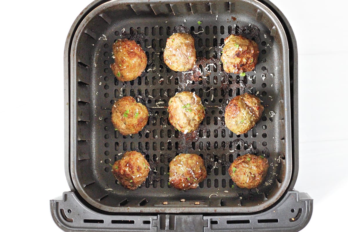 Overhead photo of baked meatballs in the air fryer topped with shredded parmesan cheese.