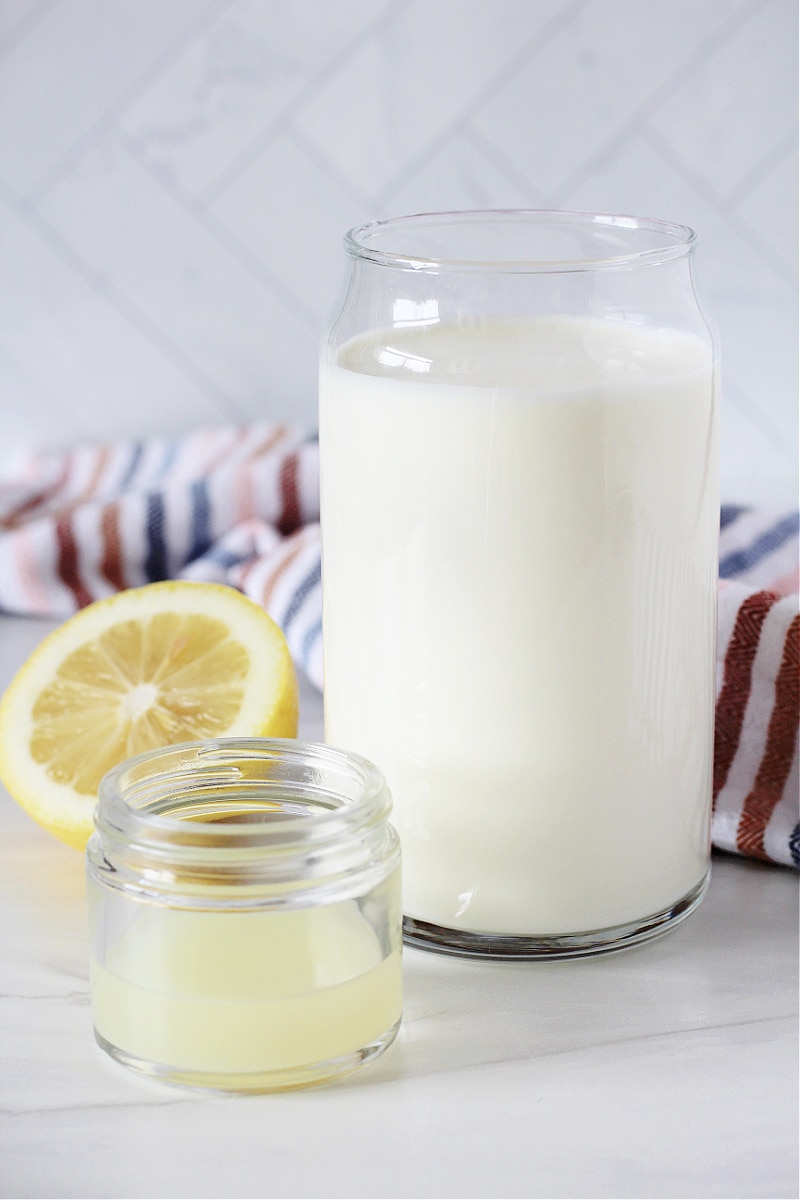 A glass of milk and a small glass jar of lemon juice to make buttermilk.
