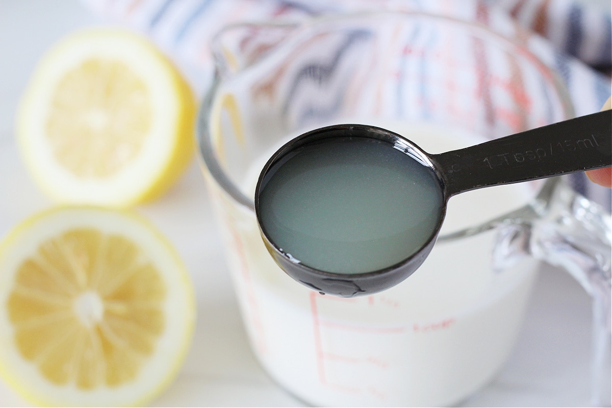 A spoon with lemon juice near a measuring cup of milk.