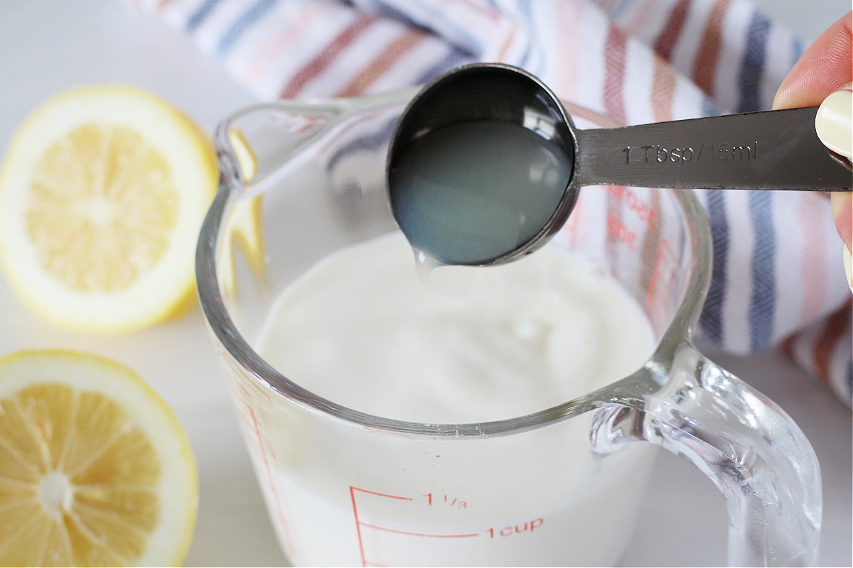 Lemon juice being poured into a measuring cup of milk.