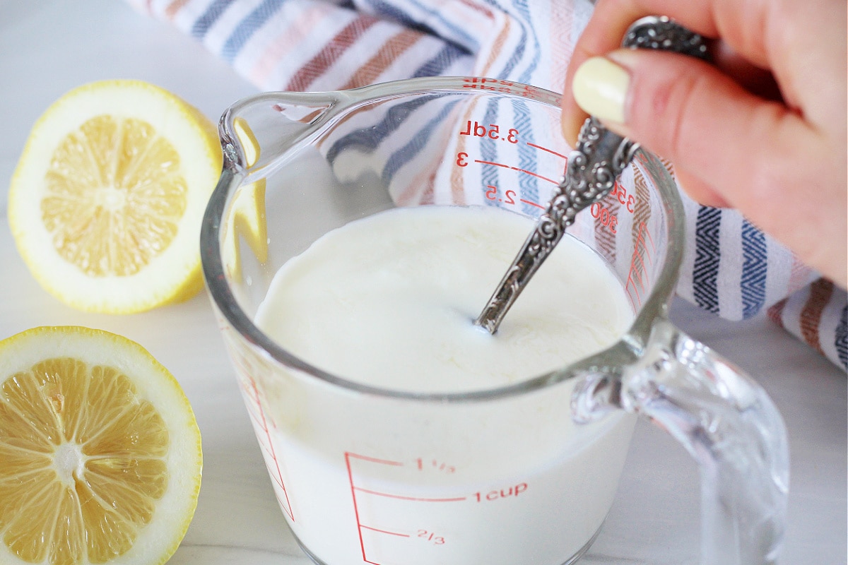 A woman's hands using a spoon to stir lemon juice into milk for buttermilk.