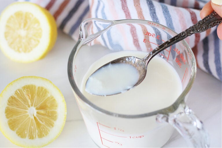 A spoon with curds of buttermilk on it over the measuring cup of buttermilk.