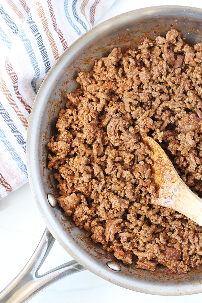 Ground beef taco meat in a stainless steel pan and wooden spoon.