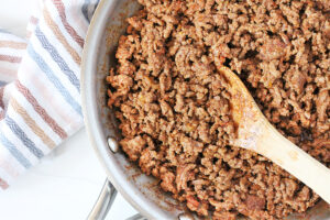 Overhead photo of ground beef taco meat in a stainless steel pan and wooden spoon.