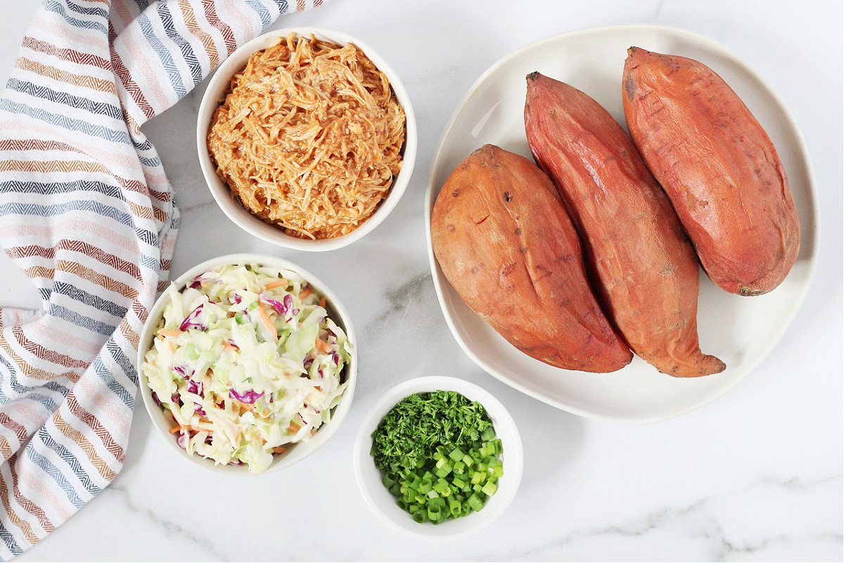 Overhead photo of cooked sweet potatoes, and bowls of shredded chicken, coleslaw and green onion.