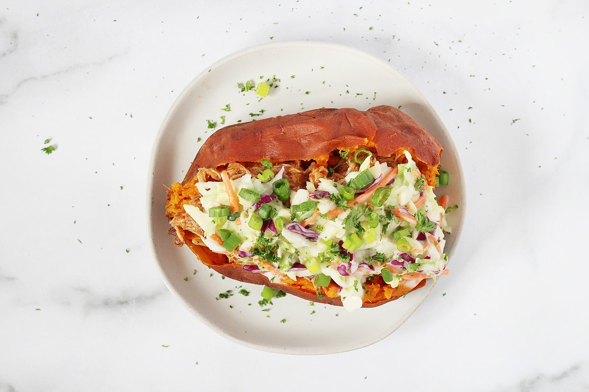 Overhead photo of a BBQ chicken stuffed sweet potato on a white plate.