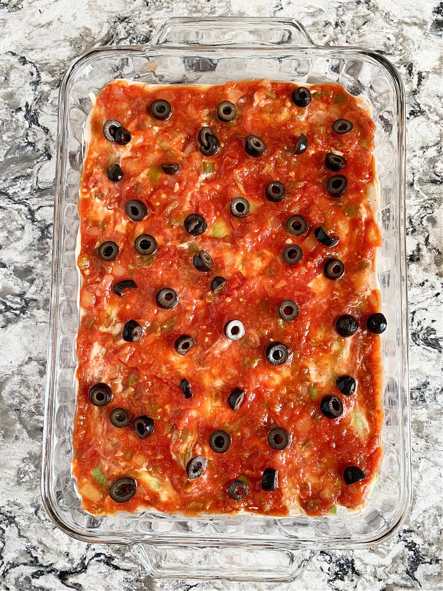 Sliced black olives sitting on salsa in a 9 layer Mexican dip.