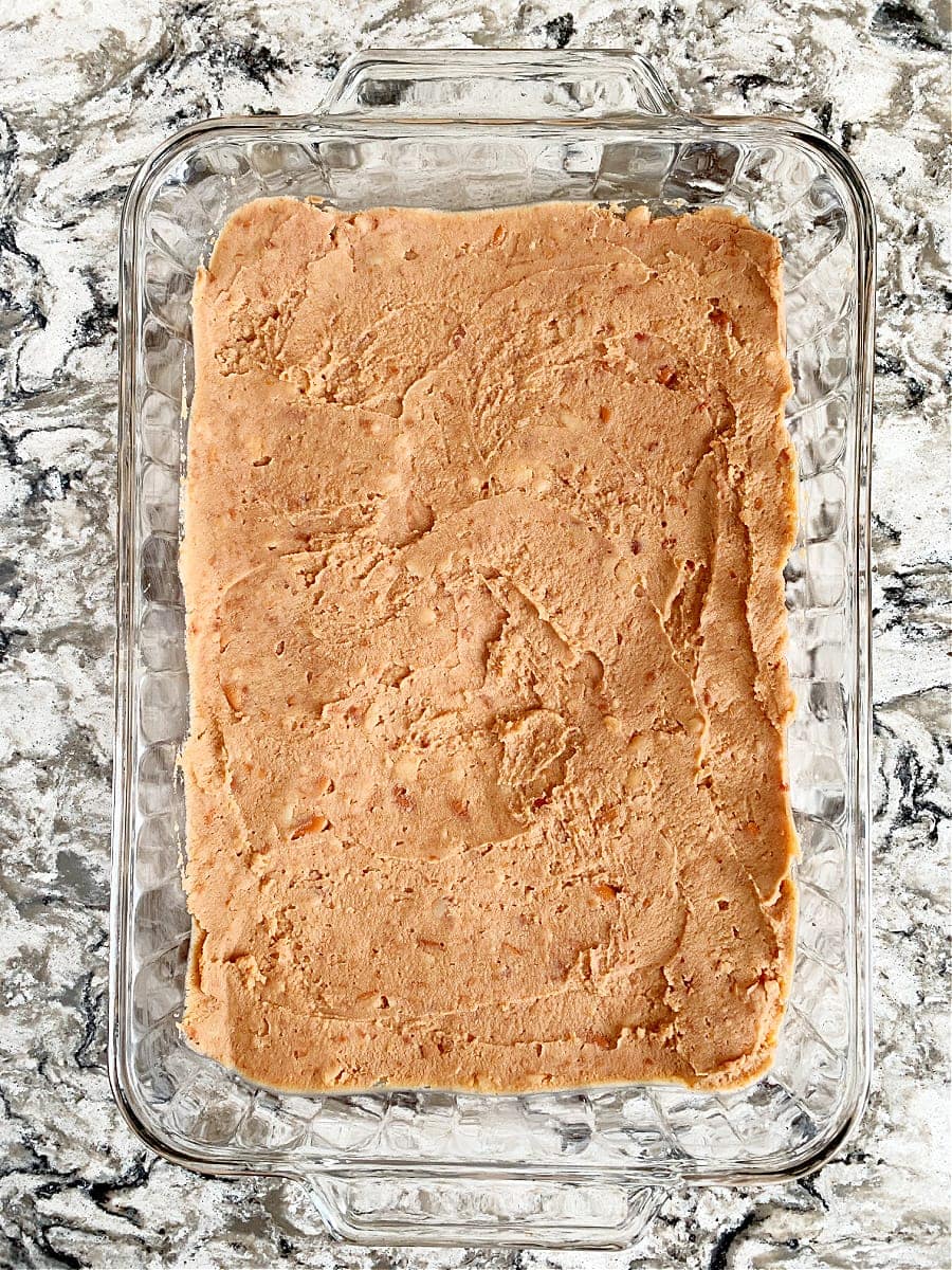 Refried beans spread evenly in a clear 9x13 glass pan. 