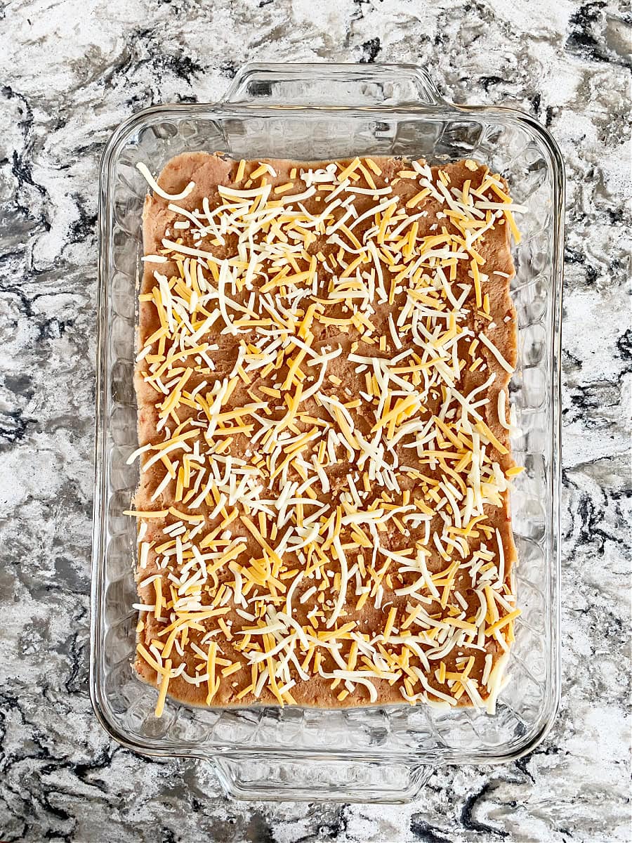 Photo of refried beans with shredded cheese on top in a pan for Mexican dip.