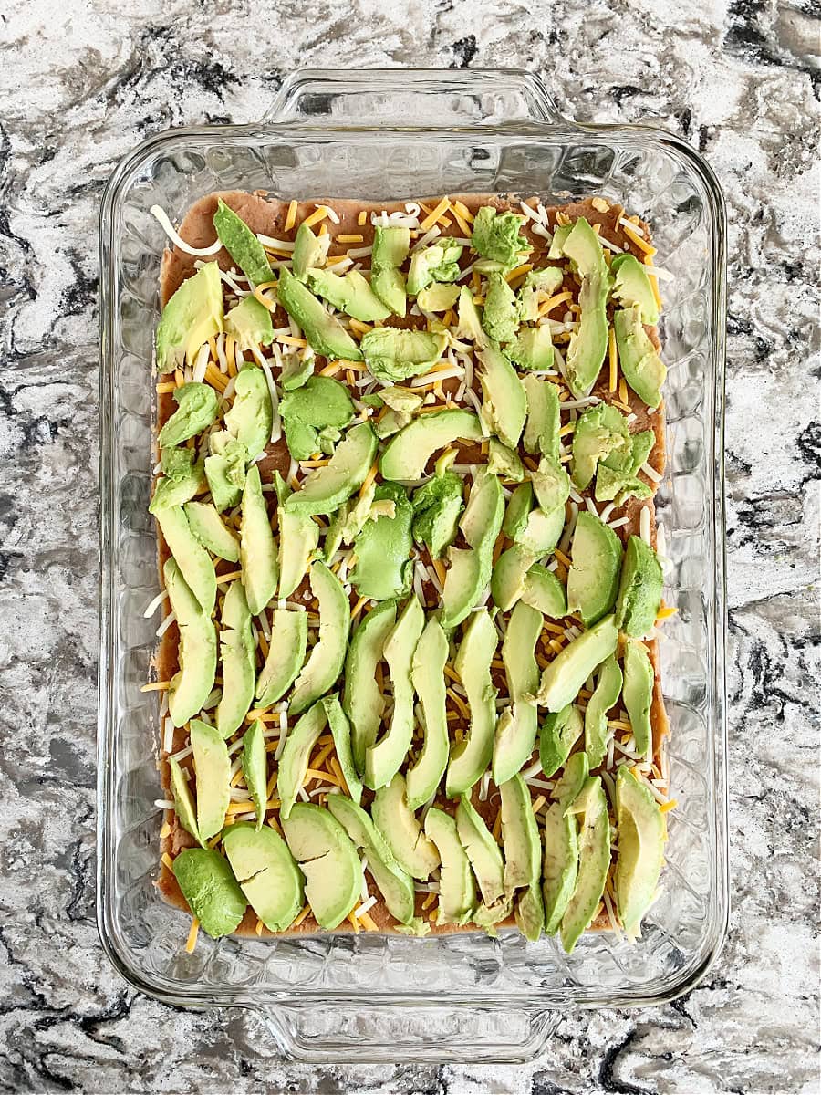 Overhead photo of sliced avocado over refried beans and shredded cheese.