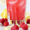 A tall glass of iced raspberry lemonade surrounded by fresh raspberries and lemon slices.