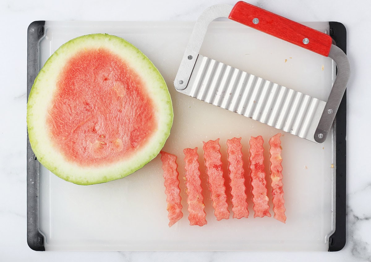 Overhead photo of a slice of watermelon, metal crinkle cutter, and watermelon fries.