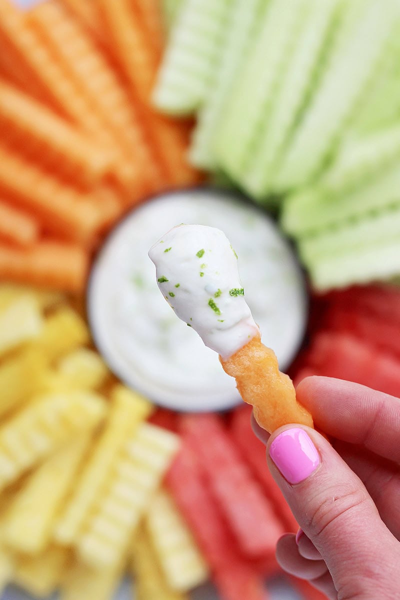 A woman's fingers holding a cantaloupe fruit fry dipped in vanilla lime yogurt dip.