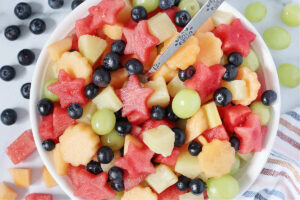 Overhead photo of a fresh fruit salad with watermelon stars and a metal spoon.