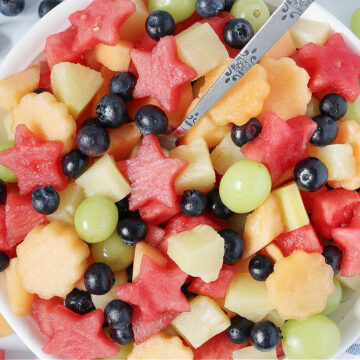 Overhead photo of a fresh fruit salad with watermelon stars and a metal spoon.