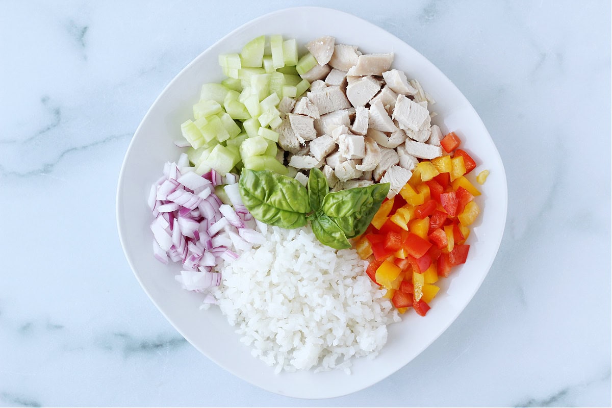 White rice, colorful bell peppers, diced chicken, cucumber and red onion in a white bowl.