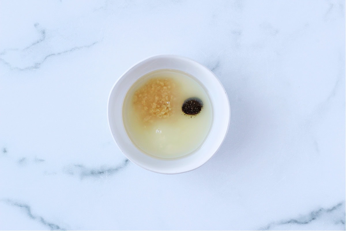 Photo of a small bowl with lemon juice, olive oil, minced garlic and black pepper.