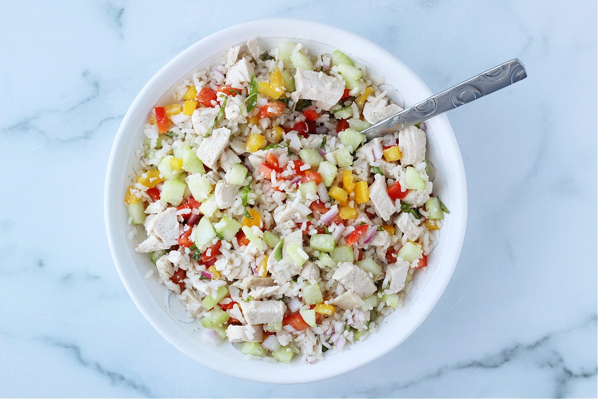 Overhead photo of a spoon in a rice salad mixed with chicken and garden vegetables.