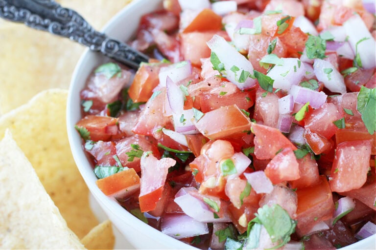 Up close photo of pico de gallo in a white bowl surrounded by tortilla chips.